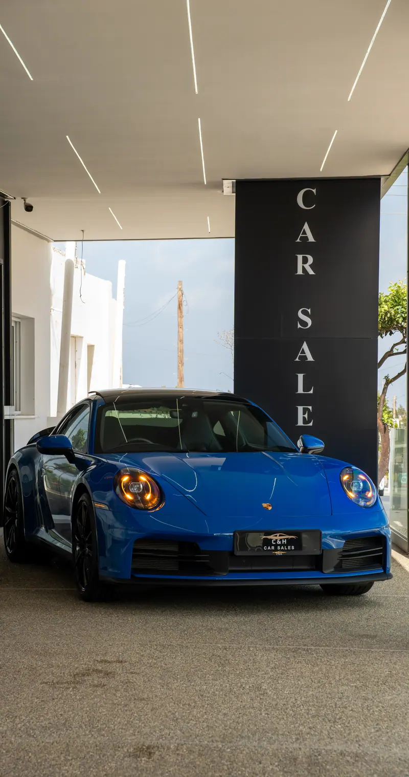 Blue Porsche 911 beside the C&H Car Sales sign under the showroom canopy