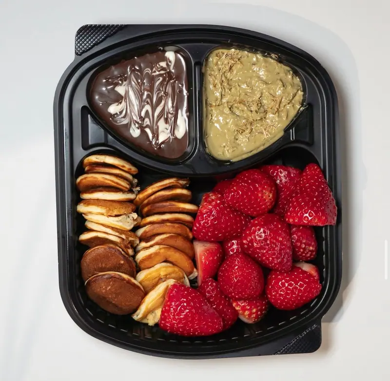 Mini pancakes and strawberries with two dipping sauces in a takeaway box